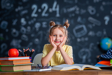 Cute happy schoolgirl with glasses. A small child is sitting at home at his desk and reading a...