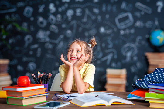 Cute happy schoolgirl with glasses. A small child is sitting at home at his desk and reading a book. Back to school. A little girl enjoys learning and doing her homework. Family education