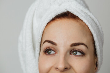Obraz premium Focuse un eyes. Close up portrait of pleasant young woman in towel isolated over grey studio background. Concept of skincare and beauty.