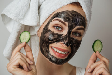 Portrait of caucasian young woman holding slices of cucumber while posing in studio with black clay...