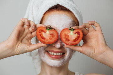 Portrait of caucasian young woman with white cosmetic mask on face and slices of tomato on eyes...