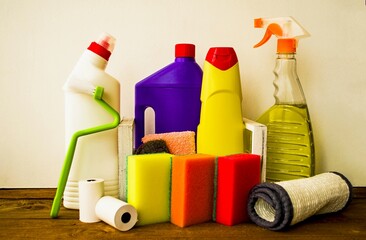On the table on a white background are hygienic and cleaning products for cleaning apartments, offices and premises, colorful bottles, sponges, a brush and napkins. Close-up photo, front view.
