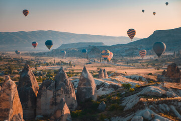 Cappadocia aerial sunrise landscape, colorful hot air balloons fly over cave house and famous fairy chimneys in Goreme national park. People enjoy wonderful aerial sun rise watching. Travel background