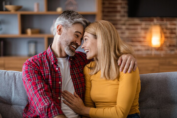Smiling happy mature caucasian male with beard and female look at each other, couple have fun together