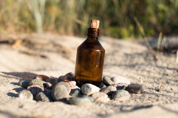 Essential oil bottle on a sandy beach with rocks. Little brown medicine bottle in nature background. Organic CBD hemp oil.