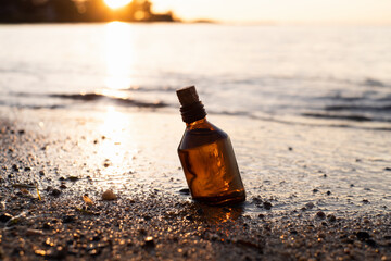 Fototapeta na wymiar Essential oil bottle on a beach in waves. Little brown medicine bottle in nature background. Organic CBD hemp oil.