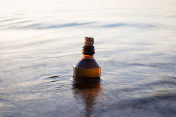 Essential oil bottle on a beach in waves. Little brown medicine bottle in nature background....