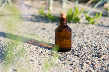 Essential oil bottle on a sandy beach. Little brown medicine bottle in nature background. Organic CBD hemp oil.