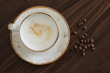 Сup of cappuccino with coffee beans on a brown wooden table, top view