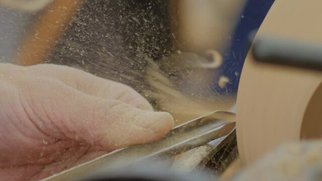 Man carpenter using chisel for shaping piece of wood on lathe machine with many sawdust, shavings at workshop - slow motion, extreme close up, macro. Carpentry, craftsmanship and manufacturing concept