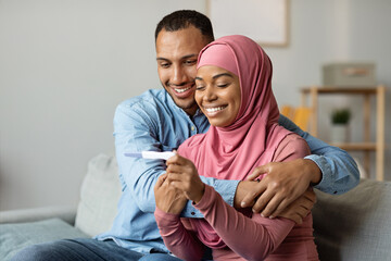 Black muslim couple checking pregnancy test while sitting on couch at home