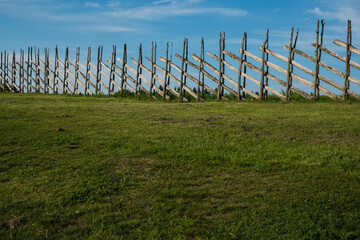 Obraz premium Handmade old wooden fence with green grass land and blue sky. Summer country style background.
