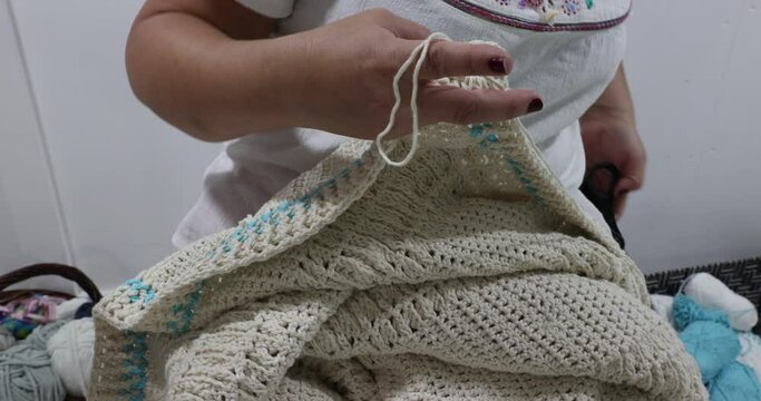 Senior adult female hands finish crocheting the edge of a beige cotton yarn blanket and cut the yarn, blue detail, original embossed crochet stitch pattern. Handmade craft creativity