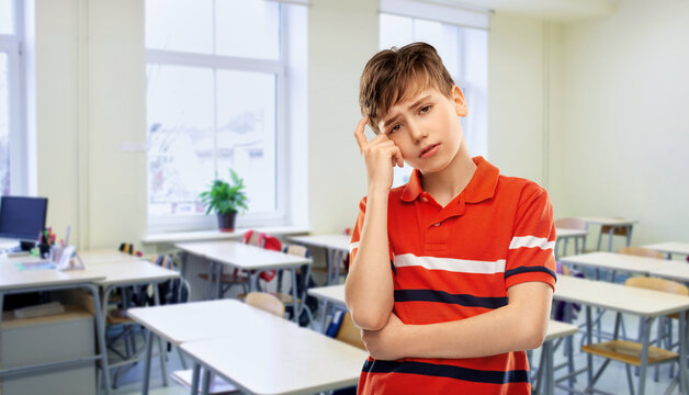 education, school and people concept - portrait of sad thinking boy in red polo t-shirt over classroom background