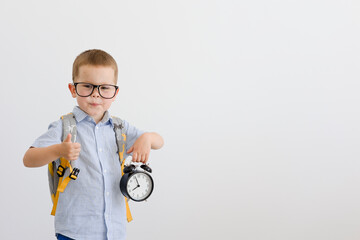 A child in glasses with a backpack on his back holds an alarm clock.