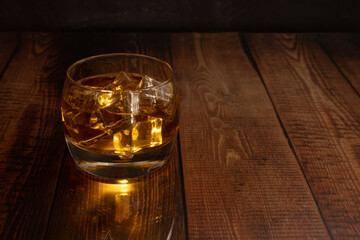 glass of whisky rum liquor with ice, lit from inside wooden table with space for text.