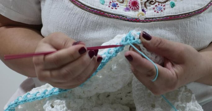 Elderly hands knitting the border in blue cotton yarn with stretchy pattern on a white crochet blanket, pink metal hook, original embossed crochet stitch pattern. Handmade craft creativity
