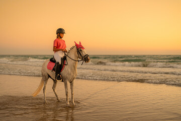 14-year-old teenager rides her white horse on the seashore wearing matching pink clothes