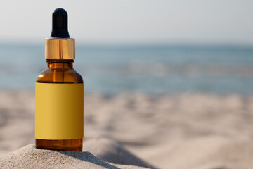 A bottle with a dropper and gold cap on the sand of the beach. Mock-up for a medicinal or cosmetic...