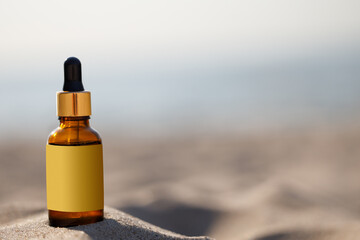 Cosmetic glass bottle of serum or essential oil on the sea beach, copy space. Liquid skincare...
