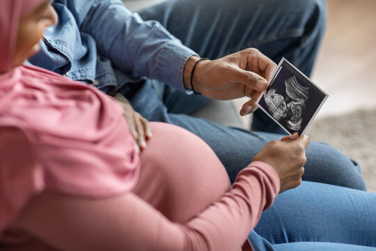 Pregnant Islamic Spouses Looking At Baby Sonography Photo While Sitting On Couch
