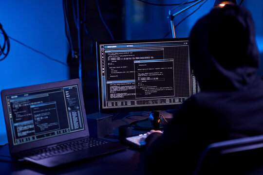 cybercrime, hacking and technology concept - hacker in dark room writing code or using computer virus program for cyber attack