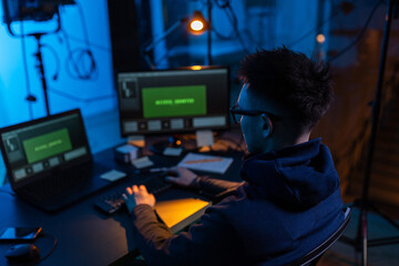 cybercrime, hacking and technology concept - male hacker in dark room writing code or using computer virus program for cyber attack