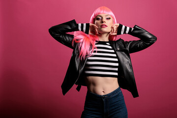 Beautiful sensual woman with pink hair wearing punk leather jacket to be trendy and advertise rocker fashion style. Female model feeling funky and attractive, standing over studio background.