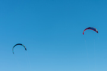 Two multicolored kitesurfing on blue sky background.
