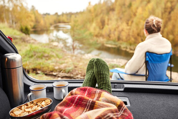 travel, tourism and camping concept - view to river from car trunk with feet in warm socks under...