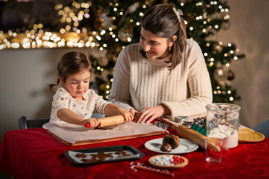 Family, Cooking And Winter Holidays Concept - Happy Mother And Baby Daughter With Rolling Pin Making Gingerbread Cookies From Dough At Home On Christmas