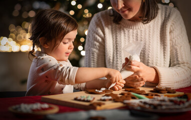 family, cooking and winter holidays concept - happy mother and baby daughter with icing in baking...