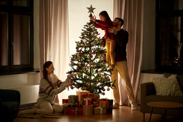family, winter holidays and people concept - happy mother, father and little daughter decorating christmas tree at home