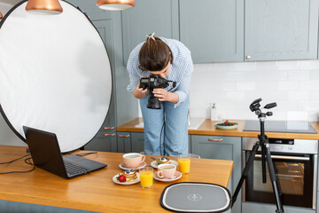 blogging, profession and people concept - female food photographer with camera photographing pancakes, coffee and orange juice in kitchen at home