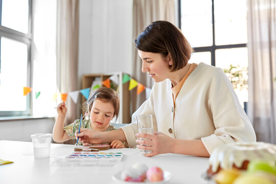 holidays, family and people concept - happy mother and little baby daughter coloring easter bunny with watercolors at home