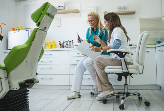 Two female dentists discuss and examine the x-ray image of the patient's teeth. 	