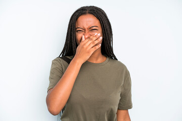 black young adult woman feeling disgusted, holding nose to avoid smelling a foul and unpleasant...