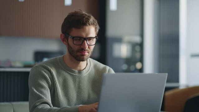 Millennial caucasian businessman sit at sofa indoor wearing eyeglasses working using laptop learn new application having questions thinking search solution having fruitful busy workday in office room