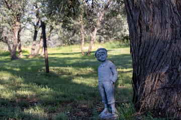 Content statue of old vintage child kid with hands in pocket in wilderness looking at camera in front of tree