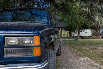 Old blue Chevy K1500 Silverado pickup from late 90s with custom black wheels sitting outdoors in nature with aftermarket headlights - obrazy, fototapety, plakaty