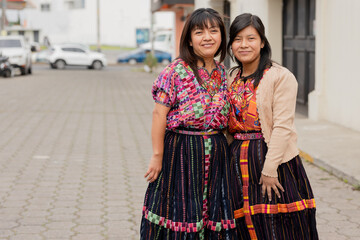 Young women with their typical Mayan dress smiling at the camera - Happy Hispanic sisters in the village in Latin America - obrazy, fototapety, plakaty