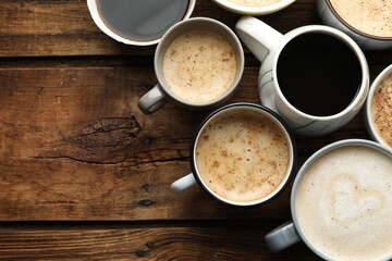 Many cups of different coffees on wooden table, flat lay. Space for text