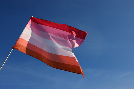 Bright lesbian flag fluttering against blue sky, low angle view. Space for text