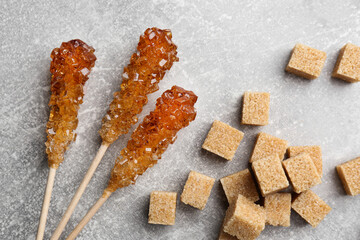 Wooden sticks with sugar crystals and cubes on light grey table, flat lay. Tasty rock candies