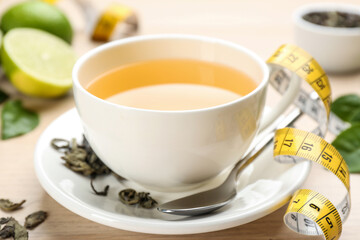 Cup of diet herbal tea, measuring tape and dried leaves on table, closeup