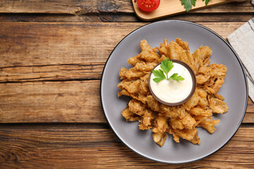Fried blooming onion with dipping sauce served on wooden table, flat lay. Space for text