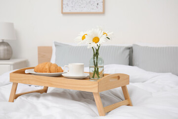 Bouquet of beautiful daisy flowers and breakfast on wooden tray in bedroom