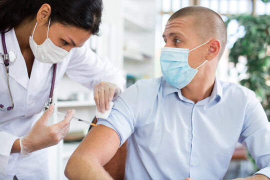 Doctor in a protective face mask giving coronavirus vaccine to pacient in modern office