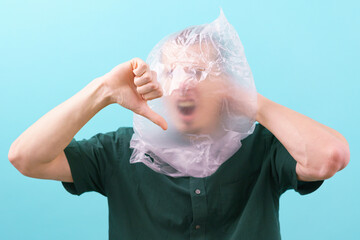 A man suffocating because of a plastic bag on his head shows his thumb down on a blue background....