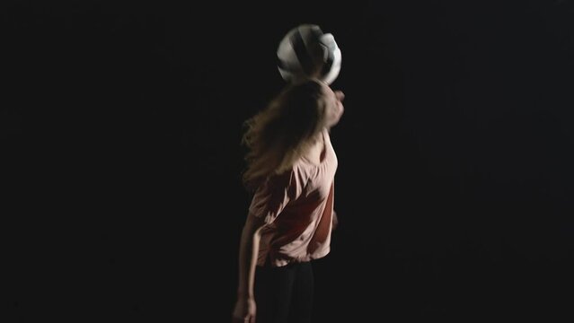 Young woman does tricks with a soccer ball on a darkly lit court